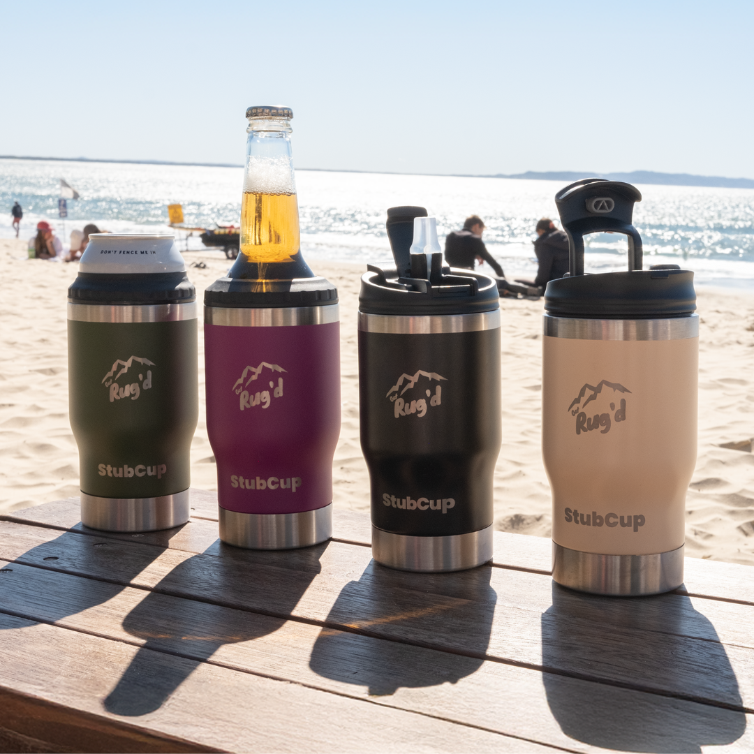 Get Rug’d StubCup 5-in-1 insulated drinkware lineup displayed on a beachside wooden table, showcasing olive green, grape, matte black, and beige colours. Each StubCup is fitted with different lids including can cooler, beer bottle holder, SwigSip coffee lid, and carry lid with handle. Perfect for hot coffee, iced drinks, beer bottles, and stubbies. Versatile travel mug, reusable cup, stubby cooler, and drink insulator – ideal for beach, camping, travel, and outdoor adventures. Features built-in bottle