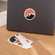 Get Rug'd car decal sticker coaster pack with mountain design on a laptop and additional stickers on a table