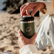 Person holding StubCup Green Stubby Cooler Coffee Cup by Get Rug'd on a sandy beach
