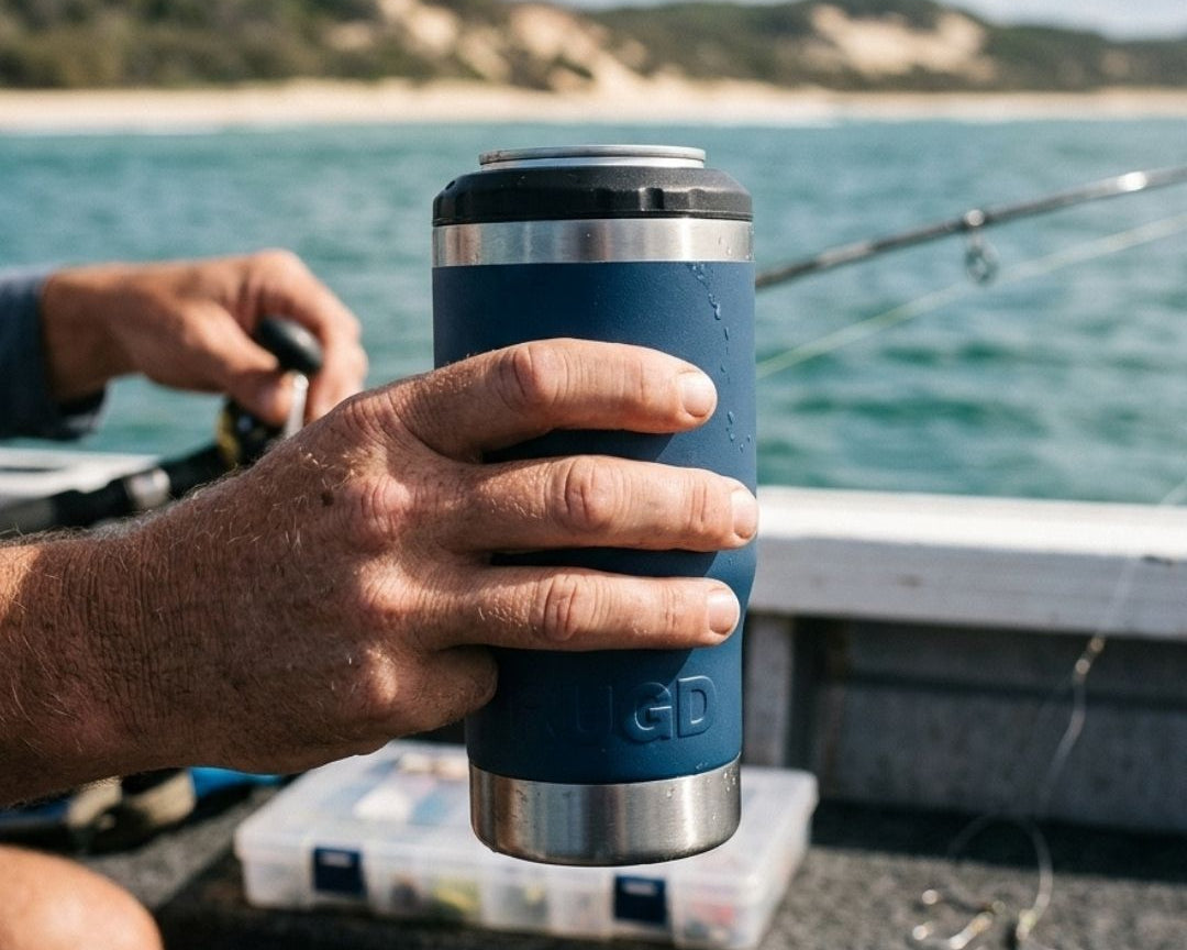 Fisher holding a navy RUGD StubCup insulated stubby cooler with a beer can on a tinnie with fishing rods and tackle box on the water