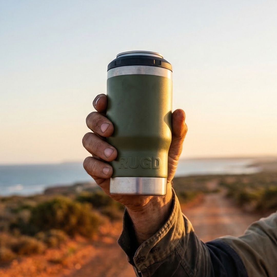 Hand holding an olive green RUGD StubCup insulated stubby cooler with SwigSip lid at sunset on an Australian coastal dirt track
