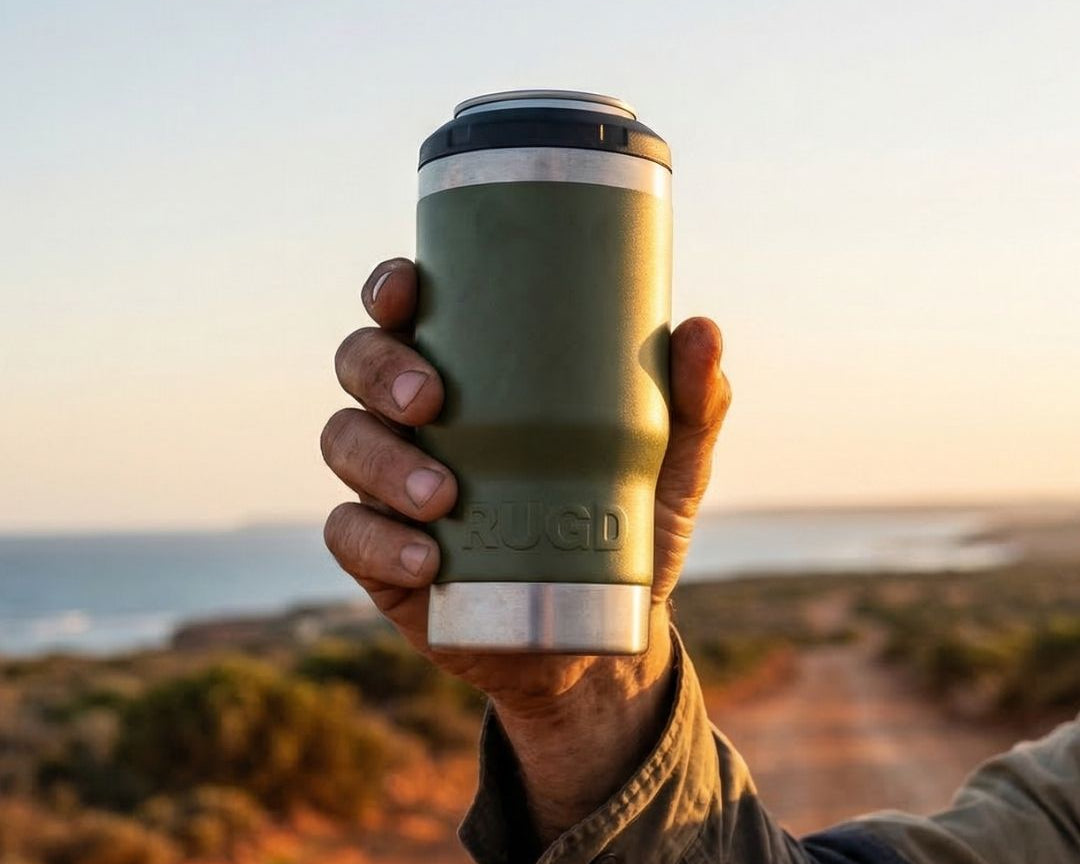 Hand holding an olive green RUGD StubCup insulated stubby cooler with SwigSip lid at sunset on an Australian coastal dirt track