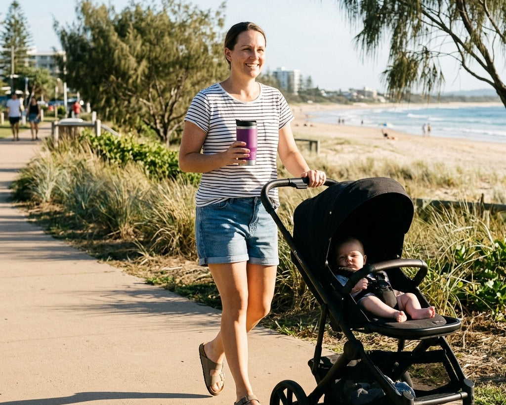 Mum holding a grape coloured RUGD StubCup insulated coffee cup while pushing a pram along a qld beachside path