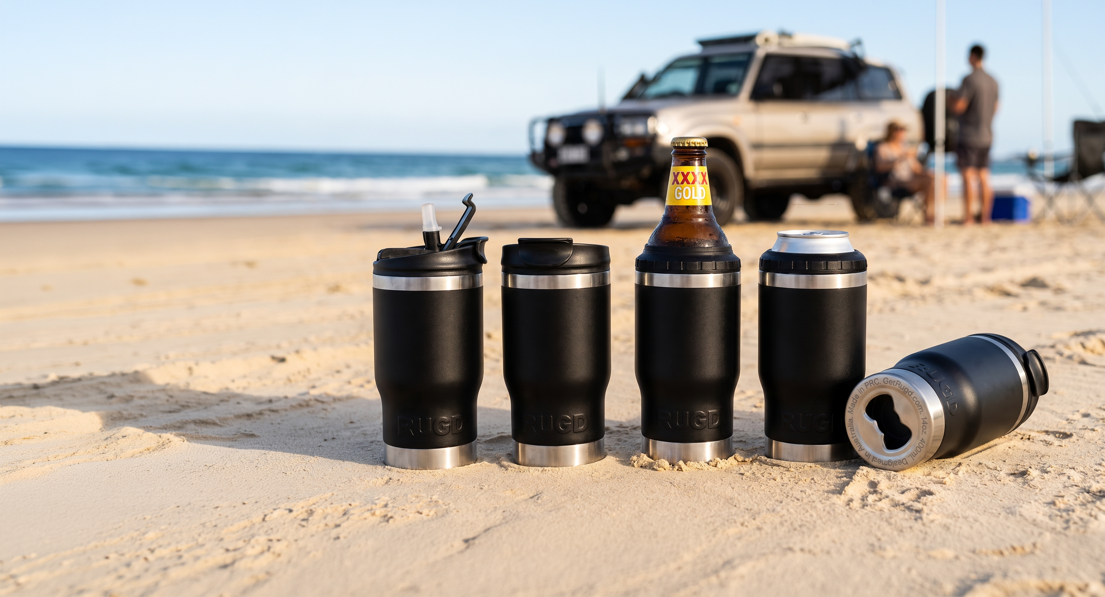 Four black insulated tumbler cups on a sandy beach, with an ocean scene and an SUV in the background. One cup is shown closed with a straw lid, one holds a beer bottle, one is empty with a lid, and one lies on its side showing bottle opener..