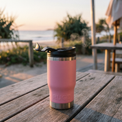 Pink insulated tumbler with a black lid on a wooden table outdoors.