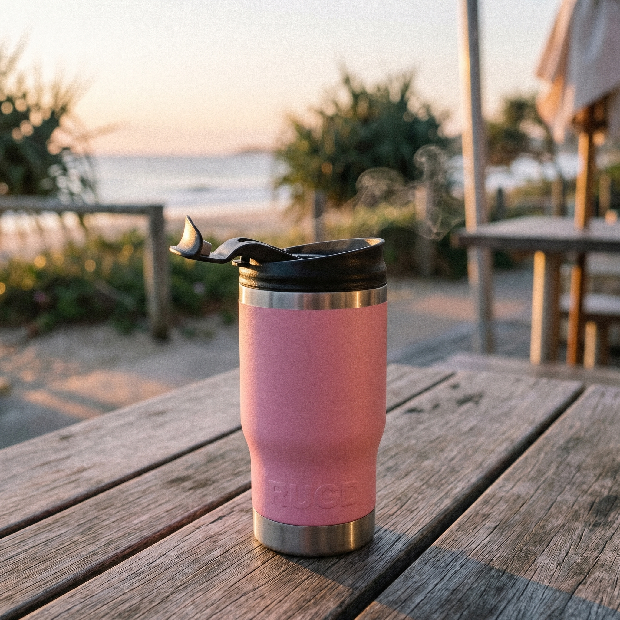 Pink insulated tumbler with a black lid on a wooden table outdoors.