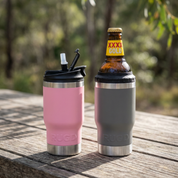 Two insulated cups, one pink and one gray, with a bottle of XXXX Gold beer on a wooden surface outdoors.