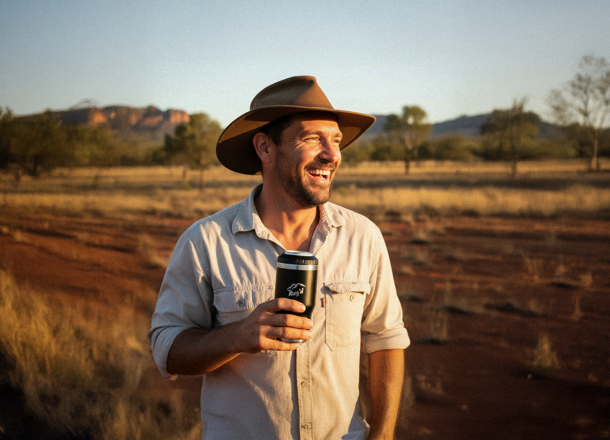 Man in a hat holding a stubcup stubby cooler coffee cup in a rural setting