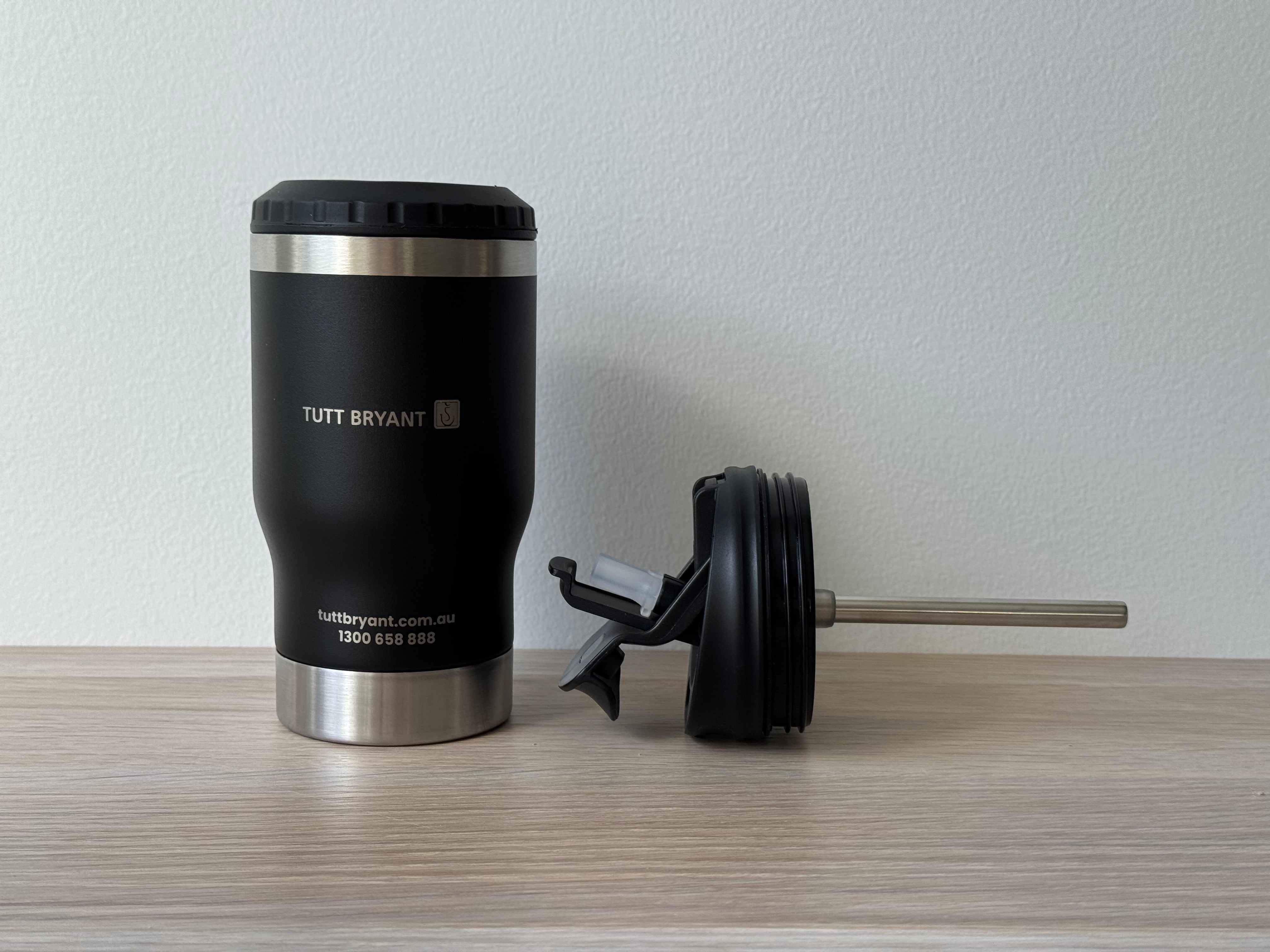 Black insulated mug with silver base and 'Tutt Bryant' branding on a wooden surface.