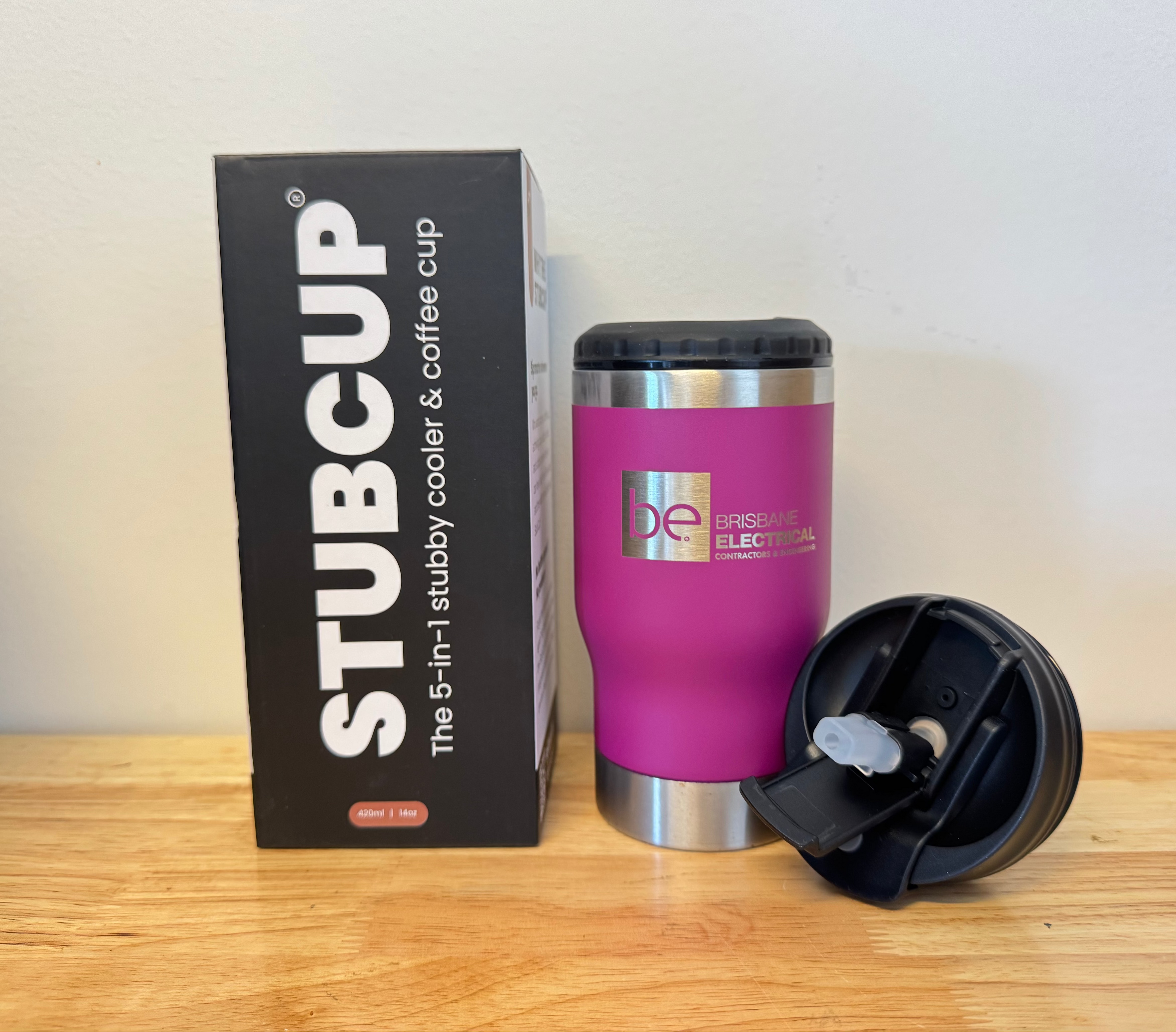 Pink thermos cup with black lid and 'STUBCUP' branding next to its packaging on a wooden surface.