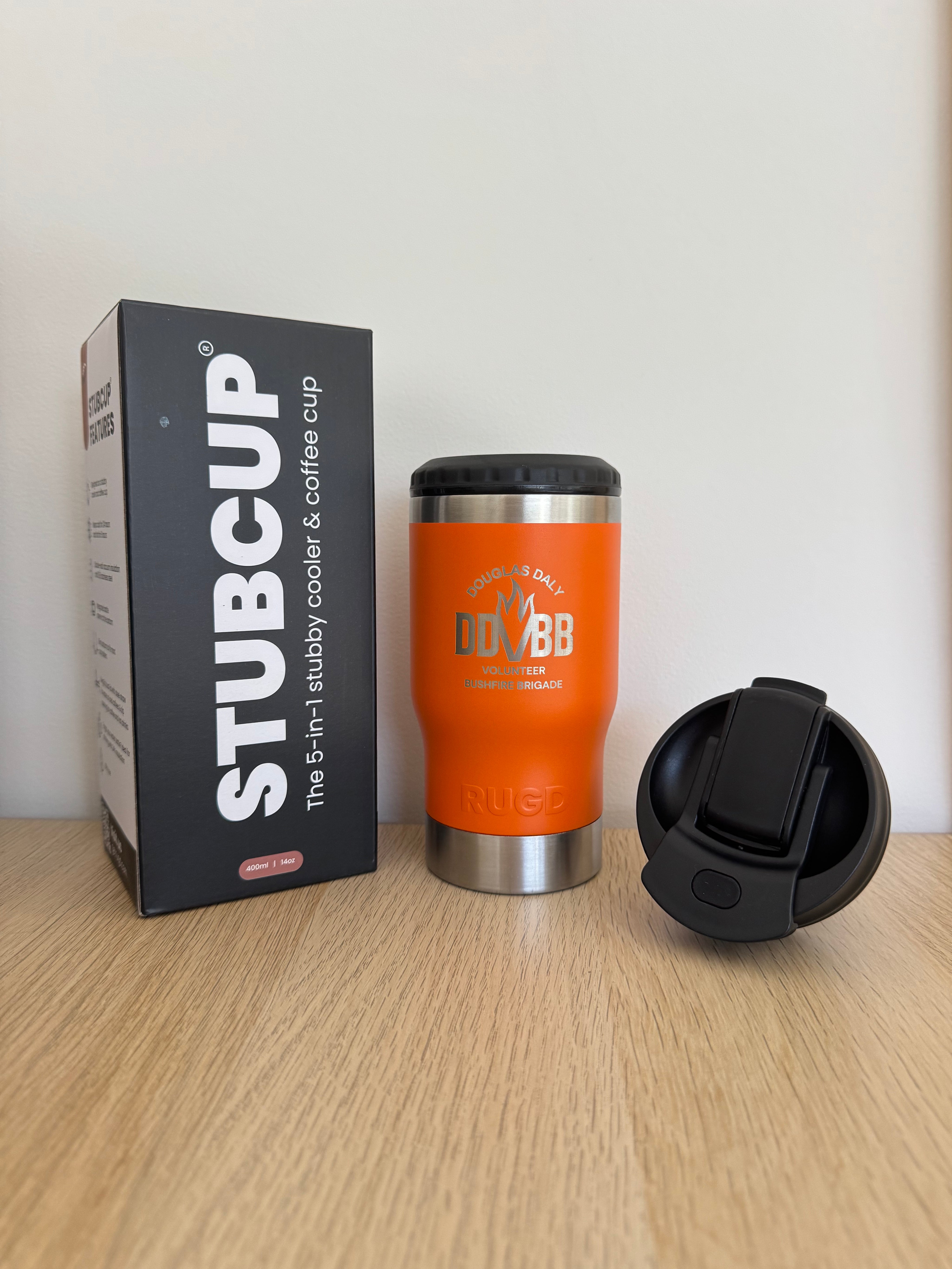 Orange insulated cup with black lid on a white surface next to its packaging box.