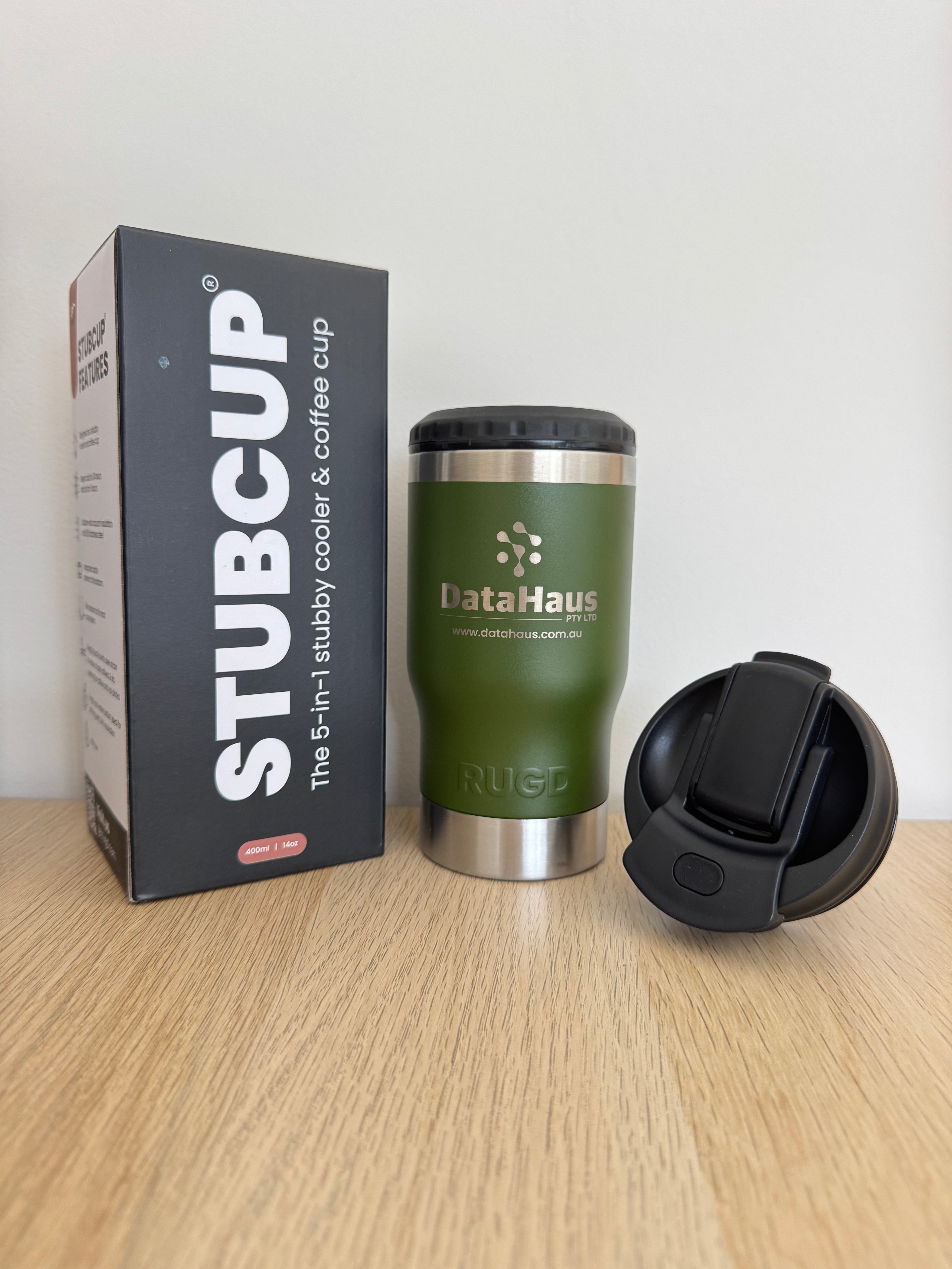 Green insulated mug with black lid on a white surface next to its packaging box.