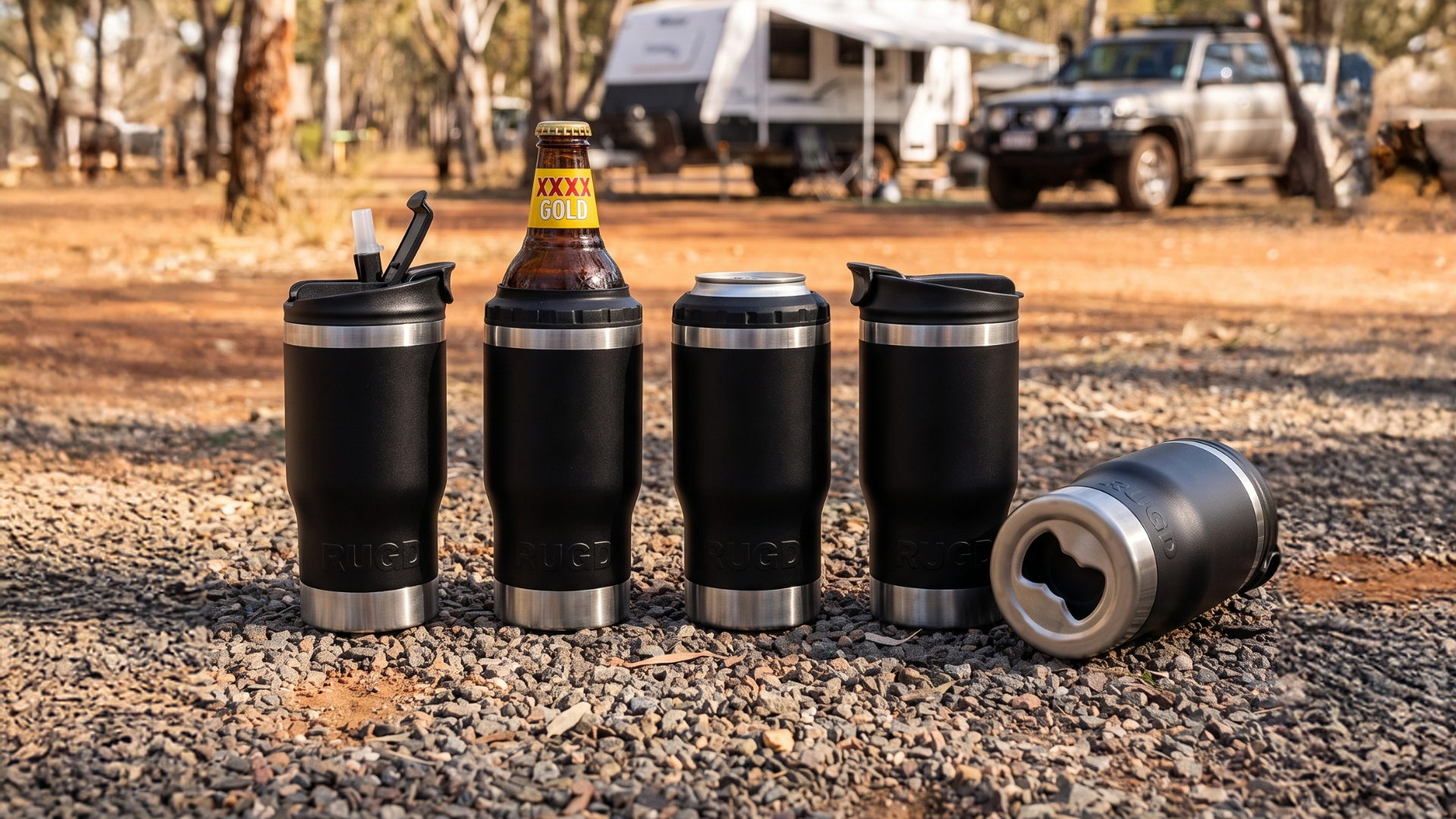 Four black insulated travel tumblers with stainless steel trim are lined up on a gravel campsite. One tumbler has a bottle inserted, and another lies on its side showing the bottle opener feature.