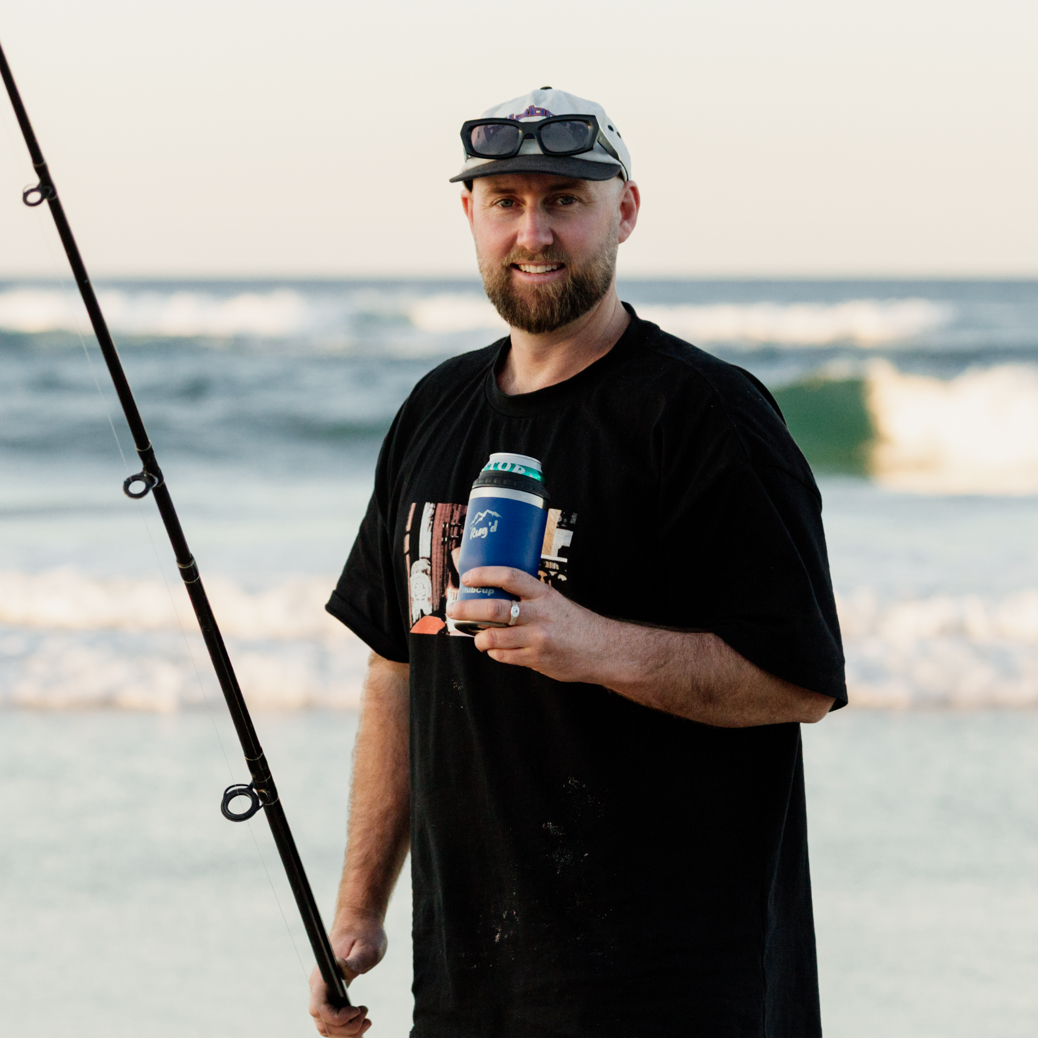 Man holding Best Stubby Cooler Coffee Cup at the beach with fishing rod in hand