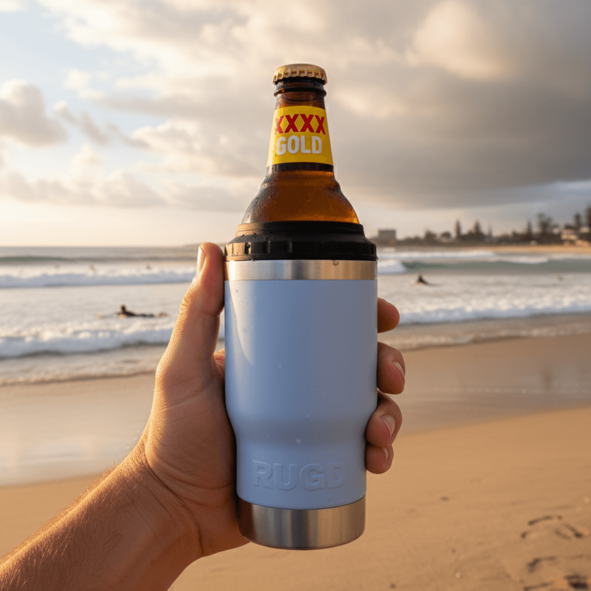 Get Rug'd StubCup insulated tumbler beer coffee in blue held by hand on a beach with waves in the background